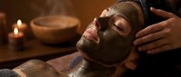 Young woman receiving relaxing chocolate face mask treatment at luxury spa with candles and wooden bowls in warm ambient lighting for skincare wellness.