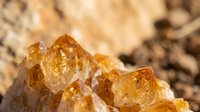 Golden amber citrine crystal cluster with natural rough texture and warm honey tones on blurred mineral background for healing and meditation practices.