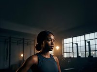 Focused female athlete in dark tank top training in modern gym with industrial windows and warm lighting, ready for workout and fitness routines.