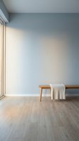 Minimalist interior corner with wooden bench, cream blanket, light blue wall and natural window light on hardwood floor for modern home design.