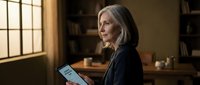 Mature Caucasian businesswoman reading tablet in warm office library setting with natural window light and wooden furniture for corporate technology concepts.