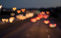 Heart-shaped bokeh lights creating romantic atmosphere on blurred city street at dusk with warm golden and red glowing effects for Valentine's Day designs.
