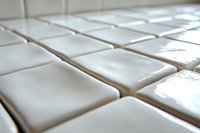 White ceramic tiles arranged in a grid pattern with shallow depth of field creating soft focus effect, highlighting texture and glossy surface finish.