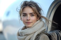 Young blonde woman with messy hair wearing beige knit scarf looking at camera with soft natural lighting and blurred urban background for lifestyle content.