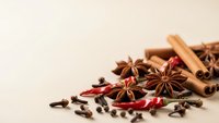 Aromatic spices including star anise, cinnamon sticks, cloves and chili peppers arranged on neutral background for culinary and cooking projects.