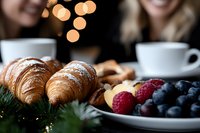 Fresh croissants and mixed berries on festive table with coffee cups and warm bokeh lights creating cozy breakfast atmosphere for holiday morning celebration.