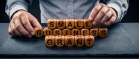 Small business grant concept with wooden letter cubes arranged by male hands on dark slate surface, symbolizing funding and entrepreneurship.