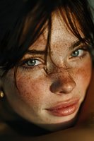 Close-up portrait of young Caucasian woman with freckles and green eyes in warm golden sunlight creating dramatic shadows on face for beauty campaigns.