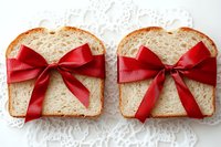 Two slices of white bread tied with red satin bows on a lace background, symbolizing food as a gift for holidays and celebrations.