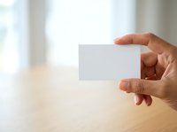 Hand holding blank white business card against blurred interior background. Corporate branding mockup for design presentations and marketing materials.