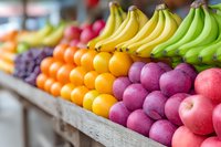 Fresh colorful fruits arranged in wooden crates at local market stall, including ripe bananas, oranges and red apples, selective focus on produce display.