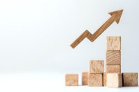 Wooden arrow rising upward from stacked blocks against white background, representing business growth, success and positive financial performance trends.