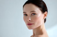 Young Asian woman with natural makeup, glowing healthy skin, and sleek dark hair against light background showcasing skincare and beauty concept.