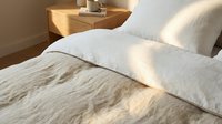 Unmade bed with white pillows and rumpled linen sheets in warm sunlight, bedroom interior design and home decor styling.