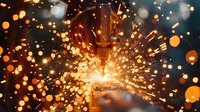 Bright orange sparks and molten metal particles explode dramatically against dark background during industrial metalworking process, creating dynamic light pattern.