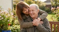Happy mature Caucasian couple embracing outdoors in garden setting with warm sunlight and residential background for lifestyle and relationship content.