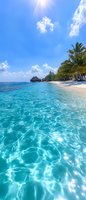 Pristine tropical beach with crystal clear turquoise water, white sand shoreline, palm trees, and overwater bungalows under bright blue sky with scattered clouds.