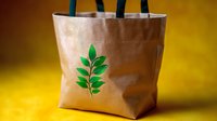 Eco-friendly reusable shopping bag with green leaf design on beige canvas against warm yellow background, promoting sustainable lifestyle and environmental care.