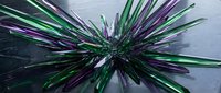 Abstract metallic spikes radiating from center in green and purple colors creating dynamic starburst pattern on dark surface for modern design projects.