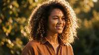 Happy young African American woman with curly hair smiling outdoors in warm golden sunlight during sunset hour for lifestyle and wellness content.
