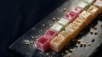 Colorful Turkish delight lokum sweets arranged on dark slate board with pistachios and spices for gourmet dessert presentation.