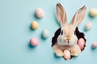 Adorable bunny rabbit peeking through hole with pastel Easter eggs scattered on light blue background, festive spring holiday composition.