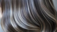 Luxurious wavy hair with silver and brown balayage highlights creating smooth flowing curves and lines in close-up view, showing modern hair coloring technique.