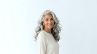 Mature woman with long silver-gray wavy hair and warm smile wearing cream-colored sweater, isolated on white background for portrait and lifestyle use.