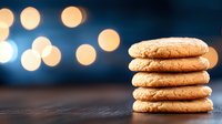 Stack of fresh homemade sugar cookies on wooden surface with blurred bokeh lights creating festive atmosphere in background. Food photography.