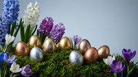 Easter eggs in metallic colors with spring flowers hyacinths and crocuses on moss creating festive holiday decoration for seasonal celebrations and greeting cards.