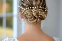 Elegant bridal updo hairstyle with pearl hair accessories and delicate twisted bun, shown from behind on blonde hair with lace dress detail.