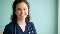 Happy female healthcare professional in navy scrubs with stethoscope smiling warmly at camera in modern medical facility for wellness campaigns.