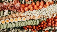Fresh vegetable and appetizer platter with sliced cucumbers, cherry tomatoes, carrots, eggs and flowers arranged in aesthetic rows for party catering.