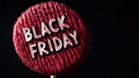 White Black Friday text on circular red knitted fabric background with dramatic lighting and shallow depth of field, creating seasonal shopping atmosphere.