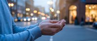 Person cupping hands in protective gesture on urban street with warm bokeh lights creating hopeful atmosphere for charity and support concepts.