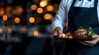 Professional chef presenting gourmet meat dish with fresh herbs and vegetables in upscale restaurant kitchen with warm ambient lighting for culinary marketing.