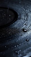 Water drops on black vinyl record surface creating atmospheric mood with circular grooves and reflective droplets in dark moody lighting.