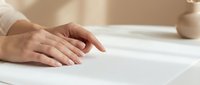 Professional hands smoothing white fabric or paper material on clean surface for crafting, sewing, or design work preparation.