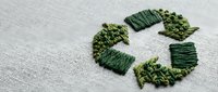 Green recycling symbol embroidered on natural linen fabric with textured stitching for eco-friendly sustainability and environmental awareness concepts.