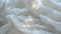 Soft wrinkled white bedding with gentle folds and shadows creating abstract patterns in morning light, clean fresh linen texture for bedroom and lifestyle designs.