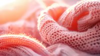 Soft knitted fabric in coral pink color with gentle folds and texture creates cozy warm background with selective focus and dreamy bokeh effect.