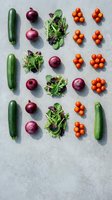 Fresh organic vegetables arranged in rows on concrete surface featuring zucchini, red onions, mixed salad greens and cherry tomatoes for healthy cooking.
