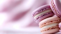 Pink and purple French macarons stacked in diagonal composition on soft blurred background. Sweet pastel colored meringue cookies with delicate texture.