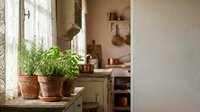 Fresh herbs in terracotta pots on rustic kitchen windowsill with natural sunlight streaming through vintage window creating cozy farmhouse cooking atmosphere.