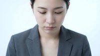 Young Asian businesswoman in gray suit looking down with closed eyes in contemplative pose against white background for corporate and professional concepts.