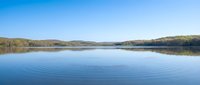 Serene lake with gentle ripples reflecting clear blue sky, surrounded by rolling hills and forest landscape for nature and outdoor recreation concepts.