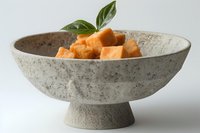 Fresh cubed sweet potato pieces in rustic ceramic bowl with basil garnish on white background for healthy cooking and meal preparation.