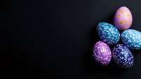 Colorful Easter eggs with floral pattern design on dark background. Festive spring holiday composition with decorated eggs in blue, pink and purple colors.