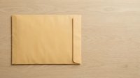 Brown kraft paper envelope lying flat on a light wooden surface, copy space on the right for text or branding in business and mail concepts.
