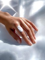Female hand with elegant white marble ring on silk fabric background with soft shadows and natural light for jewelry and accessories advertising.